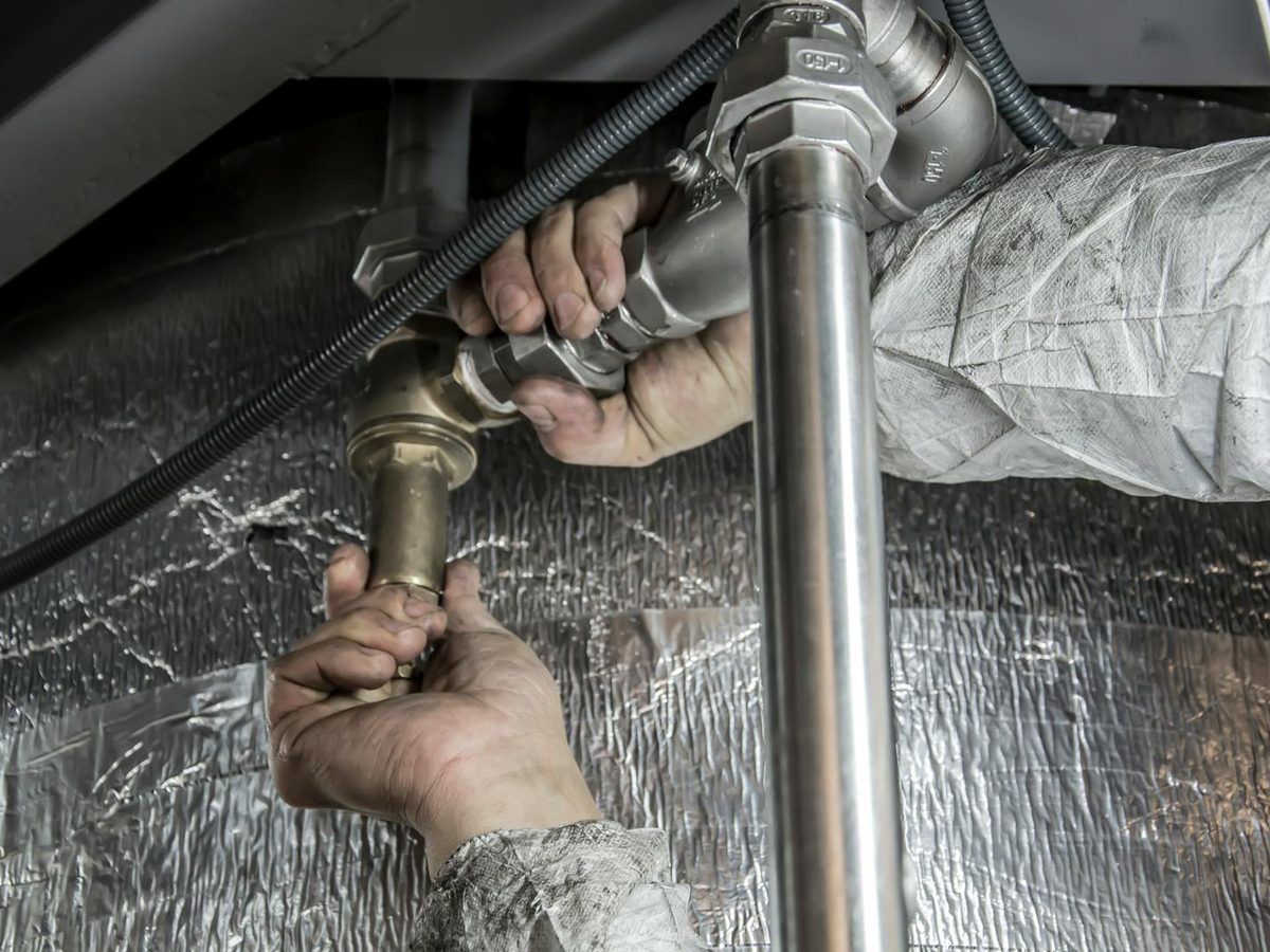 A plumber fitting metal pipework indoors with both hands visible